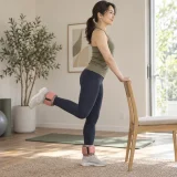椅子で支えて膝曲げ運動を行う女性
